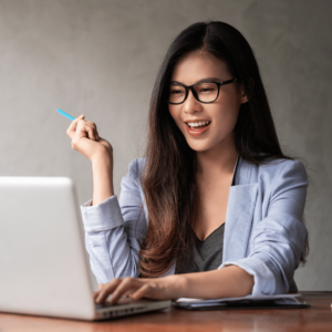 A delighted young woman sitting ina cozy home office, absorbed in her laptop screen. This image signifies the satisfaction and positivity derived from effectively managing and budgeting monthly salary in Singapore, portraying the rewarding aspect of mastering personal finance skills.