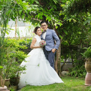 A radiant young couple capturing a joyful moment on their wedding day in a lush garden, symbolizing the start of their journey in financial planning for life events in Singapore.