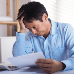 A worried Singaporean man in his home office, holding financial documents, reflecting on the importance of building an emergency fund for financial resilience amidst the economic impact of COVID-19.