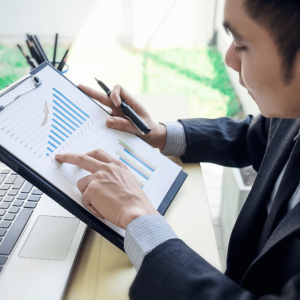 A focused man in an office environment, holding a pen and meticulously reviewing a financial chart spread out on his desk. This image emphasizes the importance of detailed examination and planning in setting effective financial goals and gauging success.