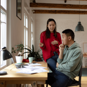 A couple in their Singaporean home engaged in financial planning discussions at their stylish home office, symbolizing their proactive approach to home-buying financial preparations.