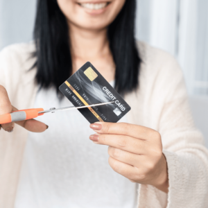 A woman assertively cutting a credit card with a pair of scissors, symbolizing a decisive step toward managing debt and cultivating a healthier credit history. This action represents an informed choice to reduce reliance on credit and promote responsible personal finance habits.