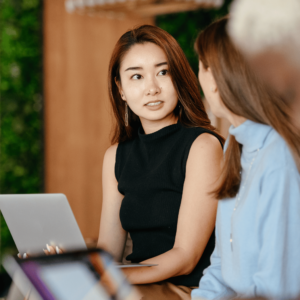 Two young professional women in Singapore engaged in a serious discussion about effective budgeting strategies and personal finance with their laptops open for referencing financial data.