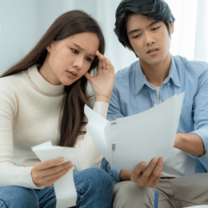 A worried young couple in a cozy living room, analyzing financial documents and bills, highlighting the importance of managing money effectively in Singapore.