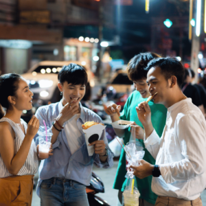 A lively group of friends enjoying various Singaporean street foods at a vibrant local night market, epitomizing cost-effective dining options in Singapore.