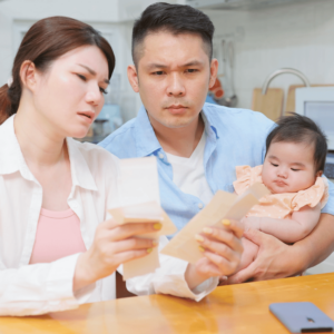 A young couple sitting at a table, discussing their child's education plan with expressions of concern and determination, while the father holds their baby.