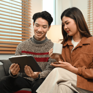 A young couple in a cozy home office, with the man studying financial data on a tablet and the woman holding a cup of coffee, symbolizing their shared engagement in regular financial reviews.