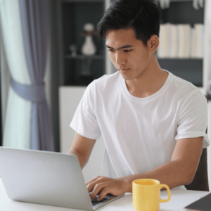 A man comfortably settled in his home office, attentively checking his finances on his laptop. A cup of coffee by his side indicates a relaxed yet focused approach to managing personal finances, reinforcing the importance of regular financial health checks in achieving prosperity.