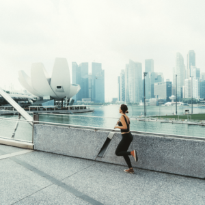 An energetic woman jogging along the Marina Bay Sands waterfront in Singapore, embodying affordable fitness and wellness activities for thrifty living.