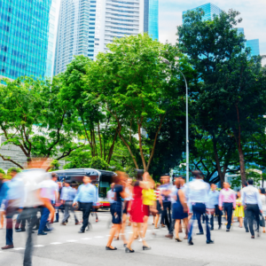 A crowd of people walking through a bustling business district in Singapore illustrates the vibrant economic activity in the city which means the increasing cost of living.