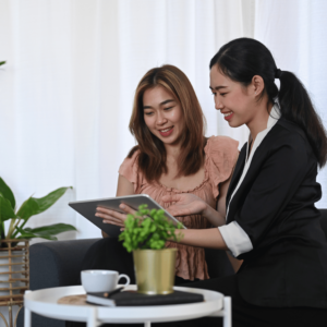 A financial advisor in a contemporary office setting discusses optimizing cash flow strategies with a young woman, showcasing relevant financial data on a tablet. Surrounding them, the desk is neatly arranged with a notebook, a coffee cup, and a small potted plant, symbolizing a serene and organized approach to financial planning and stability.