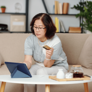 Elderly woman in a modern living room confidently using a credit card and a tablet for online transactions, embracing cashless payment methods.