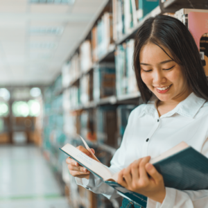 A young Singaporean woman is smiling while intently reading a book on financial literacy in a bookstore, indicating the growing interest in personal finance among youths.