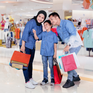 A Singaporean family enjoying a mindful shopping experience in a mall, each carrying shopping bags reflective of their well-planned budget. The young son is pointing at a desired item, illustrating the balance between wants and financial responsibility they've learned through effective budget planning.