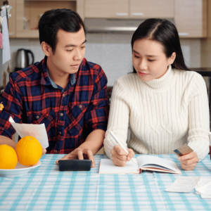 Young couple engaged in personal finance planning at a kitchen table, with the man using a calculator and the woman jotting down notes.