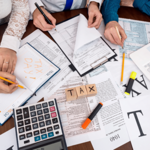 A team of focused accountants meticulously filling out forms, surrounded by an array of documents and a calculator on a large table, showcasing the detailed process of tax preparation.