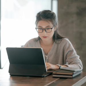 A focused young professional woman in Singapore reviewing her budget and expense reports on her laptop in a well-lit room, symbolizing the practice of frugal living and effective personal finance strategies.