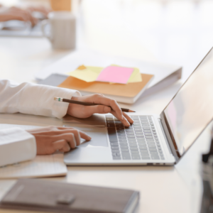 An individual at a desk with an open laptop, wallet, and sticky notes, researching various investment options and budgeting strategies online.