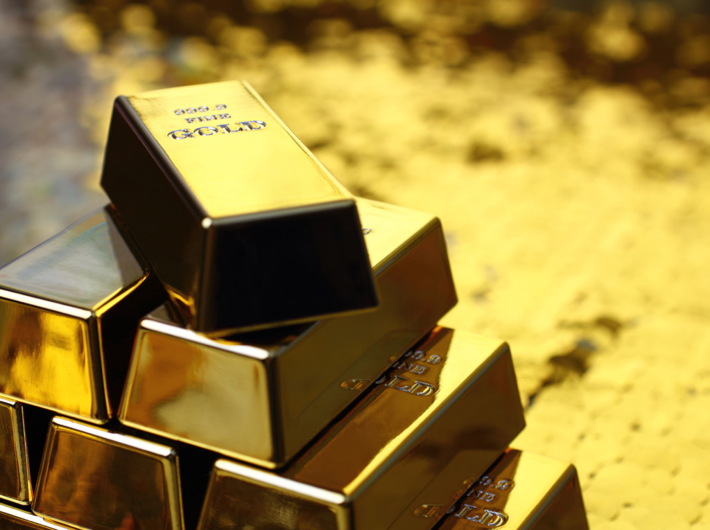 Close-up of stacked fine gold bullion bars arranged in a pyramid, polished surfaces reflecting light against a blurred golden background.